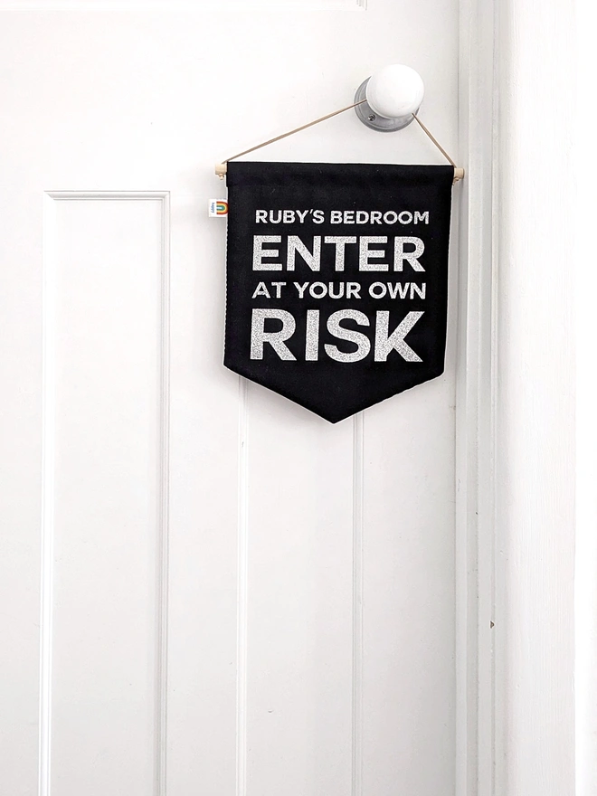 Personalised “Enter at Your Own Risk” banner for kids’ bedroom doors, handmade black fabric wall hanging with custom name design.