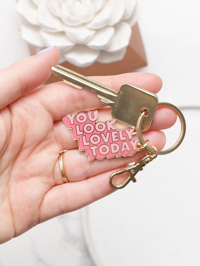 Hand holding a Pink enamel keyring with 'You Look Lovely Today' design