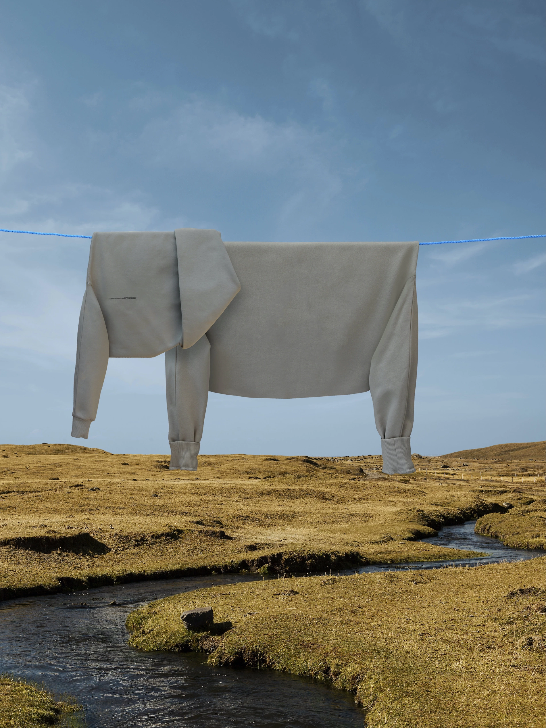 Elephant made out of clothes hung on a line above a river meandering through green fields