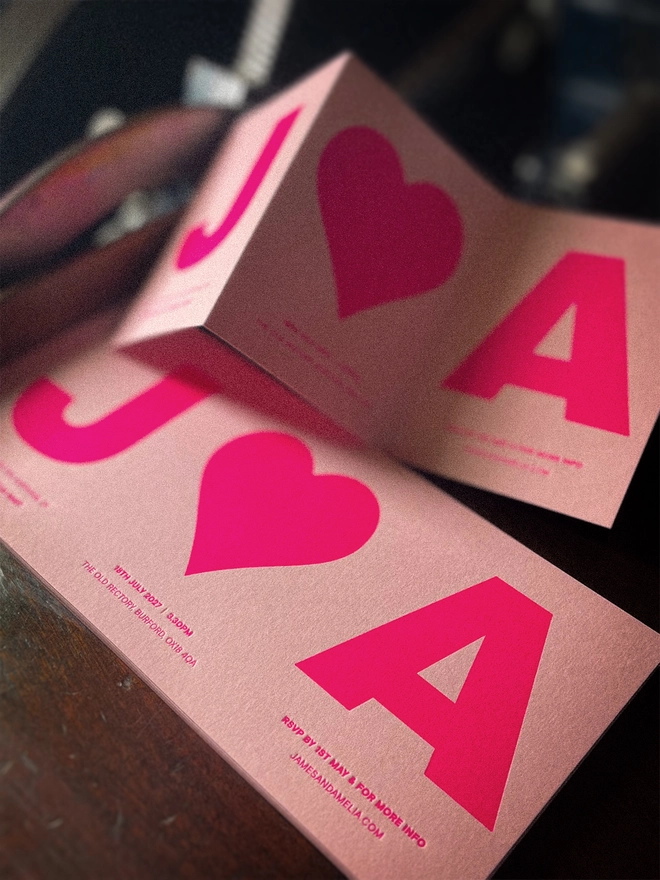 Luxury bespoke Amour wedding invitation shown open and folded, with personalised initials and heart letterpress printed in vibrant fluorescent pink on Candy Pink Colorplan.
