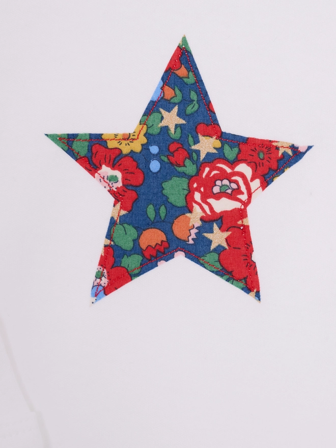 a christmas liberty print starry print star white bodysuit, close up on the appliqué stitching 