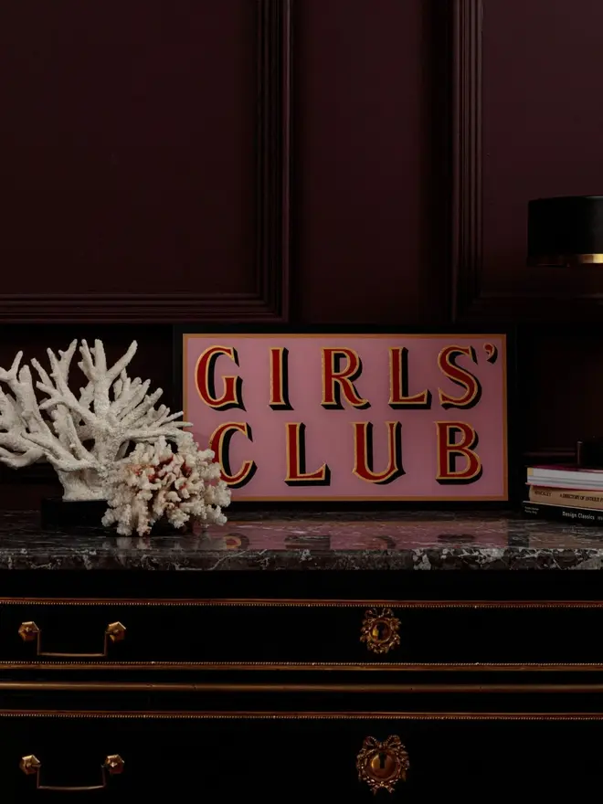 girls club pink hand painted sign. sign propped up on mantelpiece.