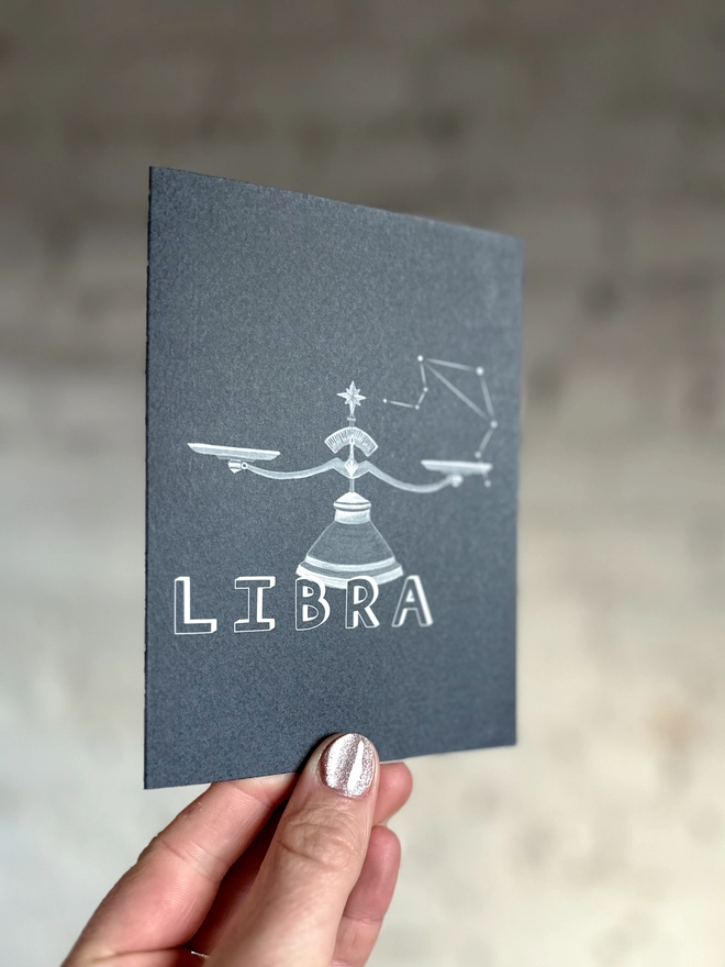  a greetings card featuring a greyscale illustration of a zodiac style set of scales with the text “LIBRA”