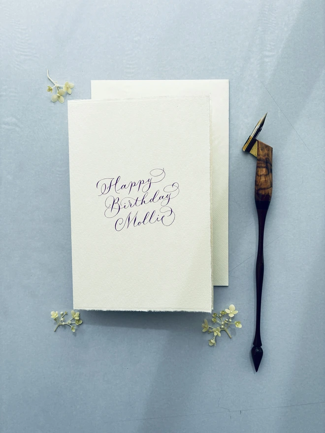 Calligraphy birthday card and envelope shown with a decorative wooden pen