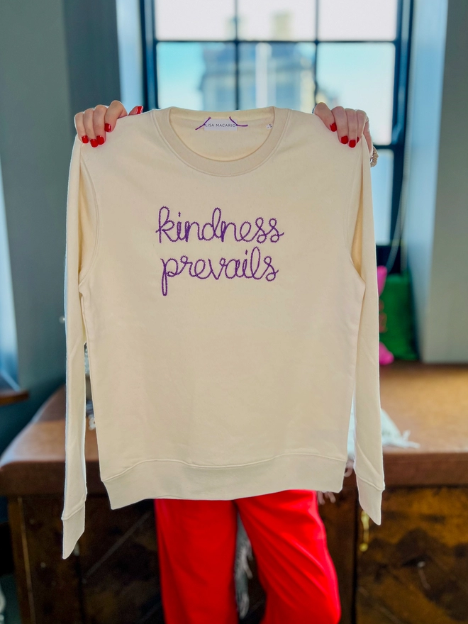 Lisa Macario in her studio holding a natural sweatshirt embroidered with kindness prevails