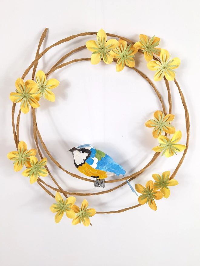 wall art sculpture of a handmade blue tit bird, perched on a wreath of yellow flowers