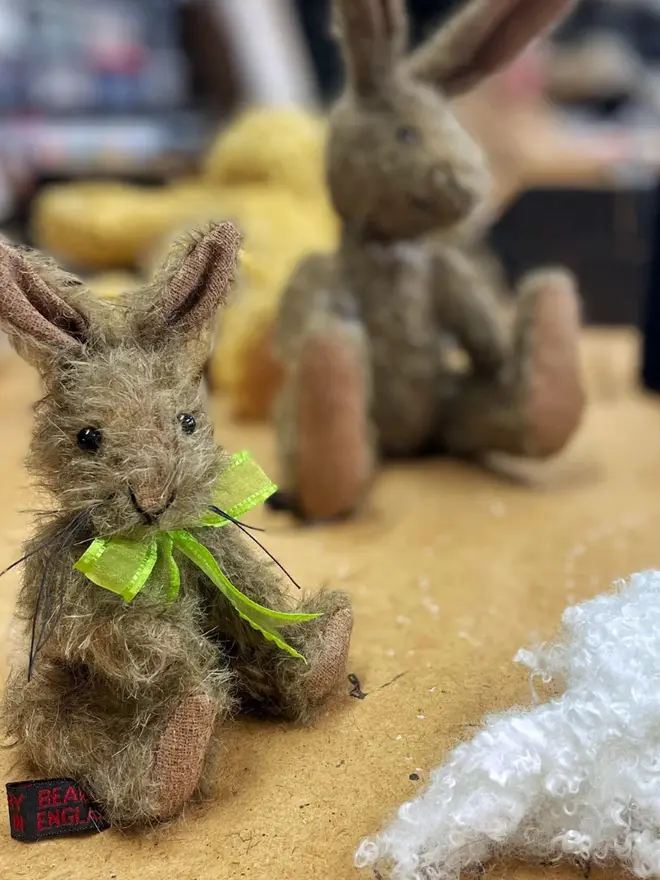 Handmade brown stuffed rabbit with long ears and a green ribbon bow sitting upright against a wooden table.