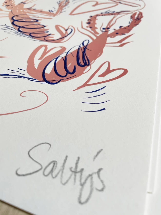 Close up of a Salty’s pencil signature, in the bottom right corner of every print. Also in shot is a pink cartoon langoustine and a heart in pink, with blue extra lines for movement, 