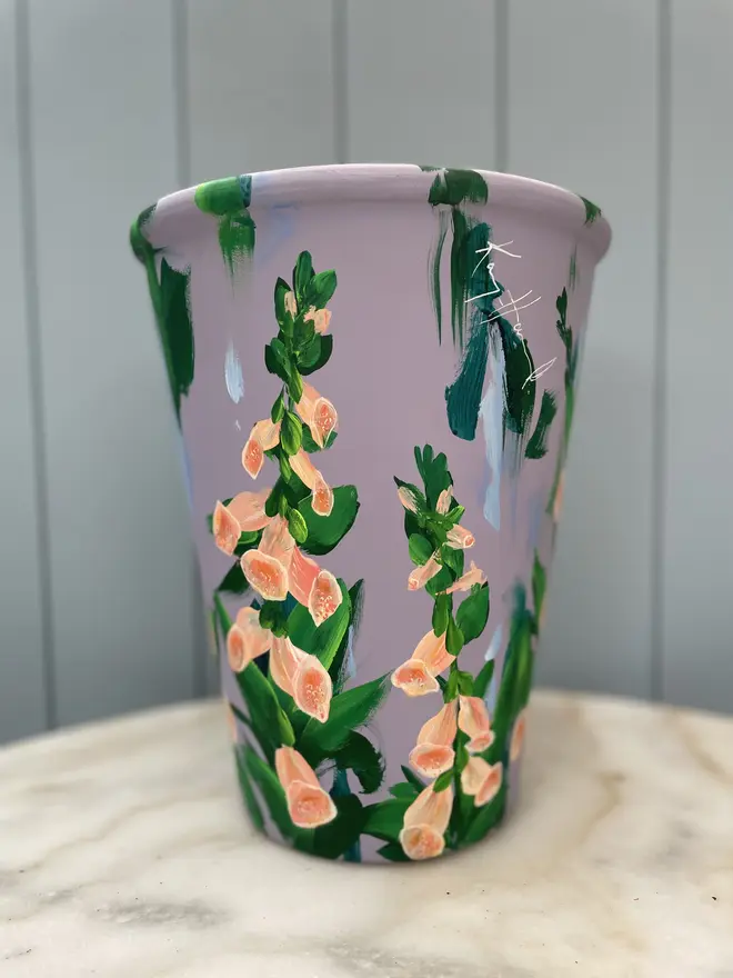 Unique hand-painted terracotta pot featuring apricot foxgloves on a lilic background