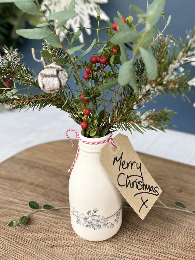 A handmade ceramic bottle filled with foliage and a Merry Christmas tag ready for gifting