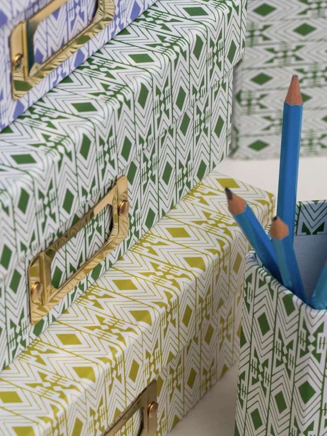 Tijan Lidded Portfolio Box, a collection of colourful portfolio boxes stacked on a plain surface. They are accompanied by a pencil pot. 