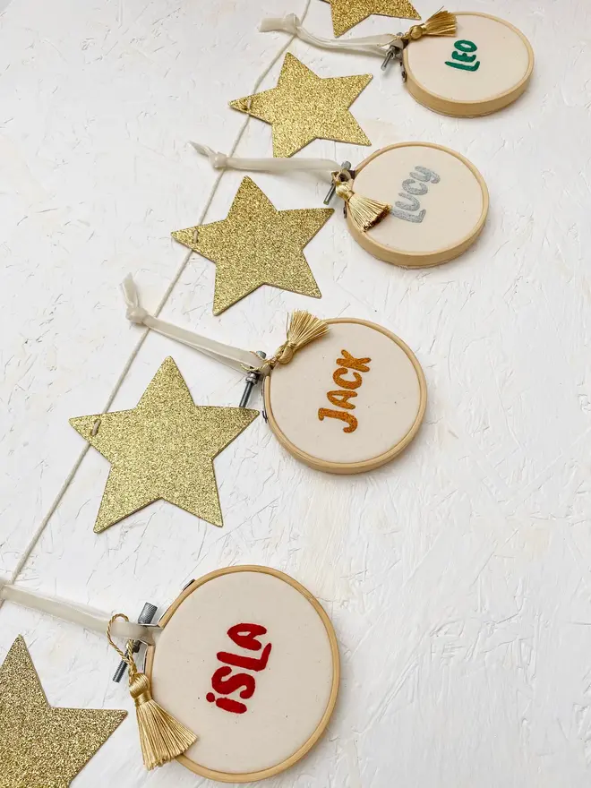 personalised name embroidered hoop bauble. set of 4 embroidered hoop baubles strung up on white wall.