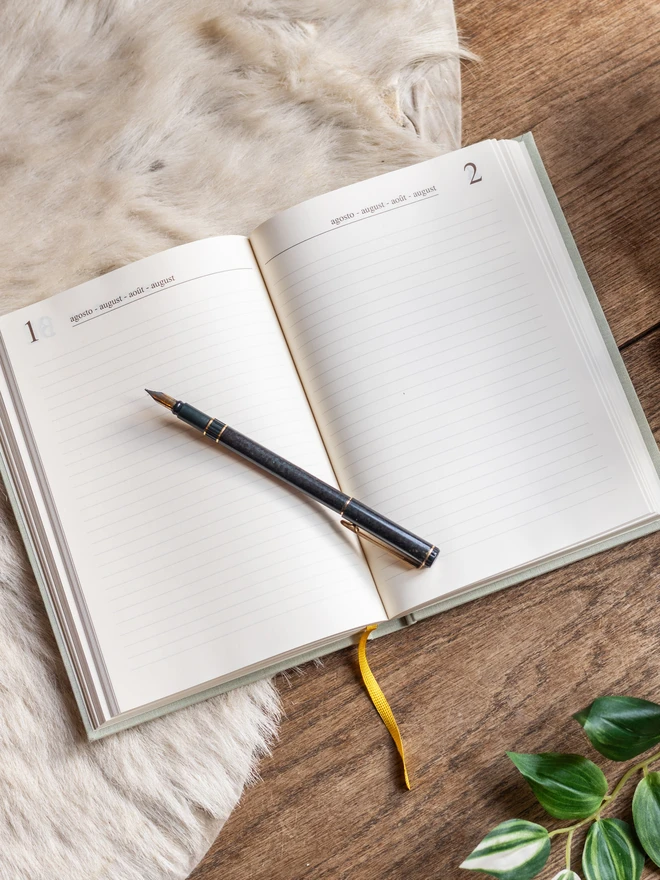 A linen-covered personalised diary lies open showing cream pages on a fur rug.