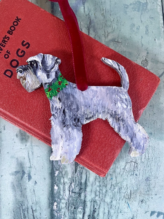 Miniature Schnauzer Hand - Painted Christmas Decoration hung with red velvet ribbon and placed on a red book about dogs