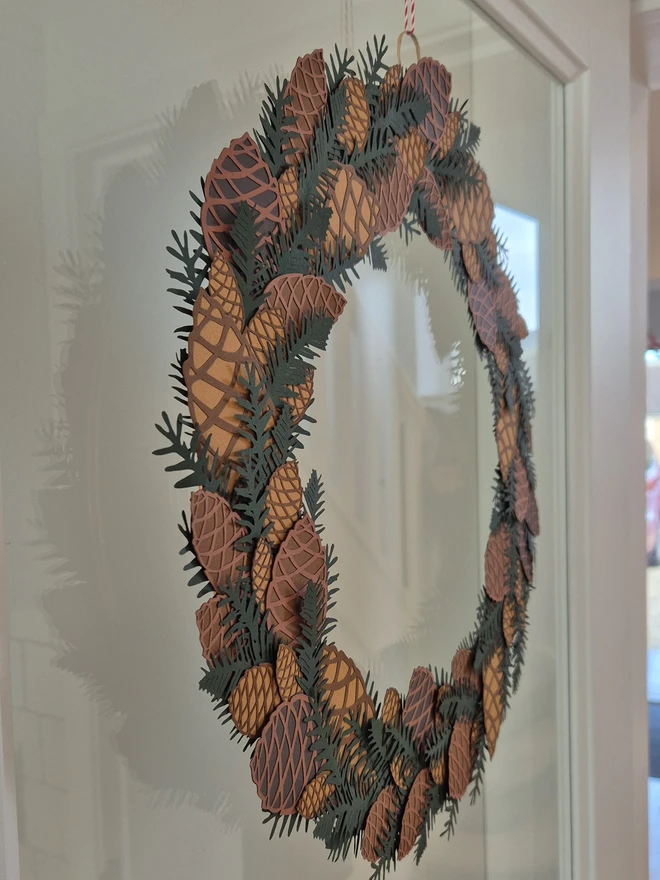 Papercut Pinecone Wreath shown side on hanging on glass door