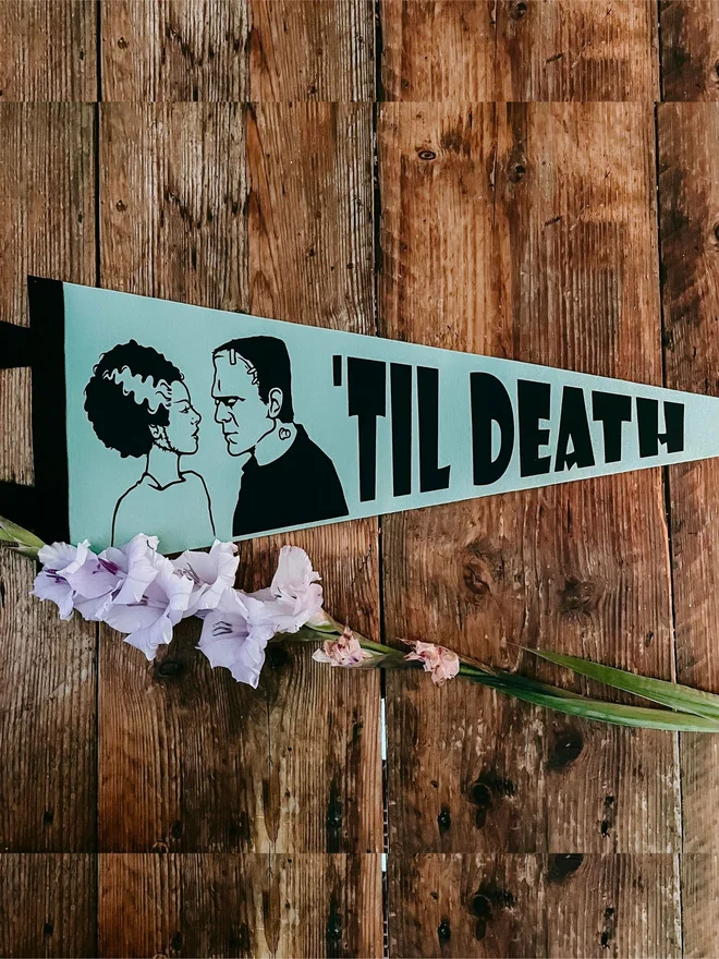 a green and black felt pennant with the image of Frankenstein and his Bride on, and the words Til Death