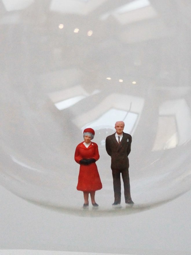 Miniature figure of Queen Elizabeth and Price Phillip in a glass Christmas bauble - close up 