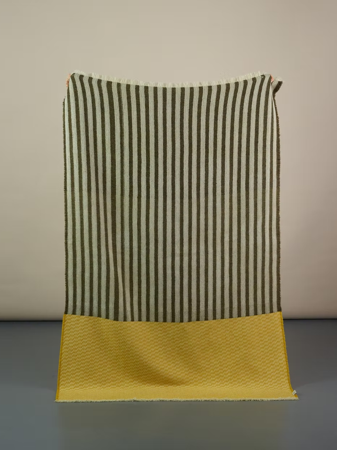 hiolair lambswool blanket. a yellow and brown striped blanket photographed against a plain wall.