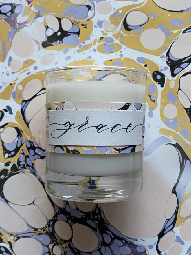 Hand Poured Scented Candle With Personalised Marbled Label seen on marble paper.