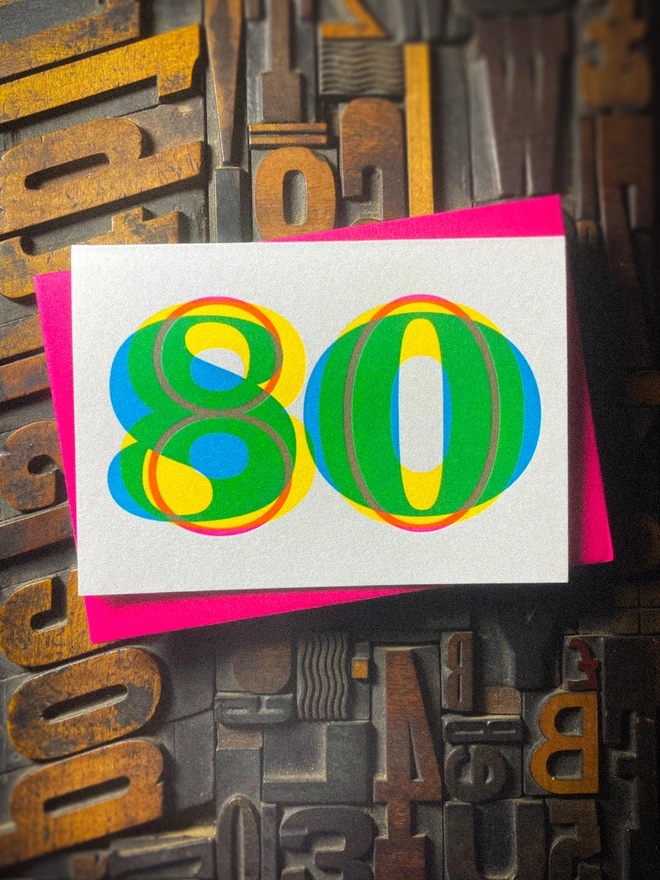 Handmade letterpress 80th birthday card featuring bold overlapping numerals printed in vibrant fluorescent cyan, magenta and yellow inks. Each card is individually hand printed using traditional letterpress techniques on luxury paper stock, creating a beautifully tactile finish with a subtle deboss and rich layered colours inspired by the CMYK printing process.