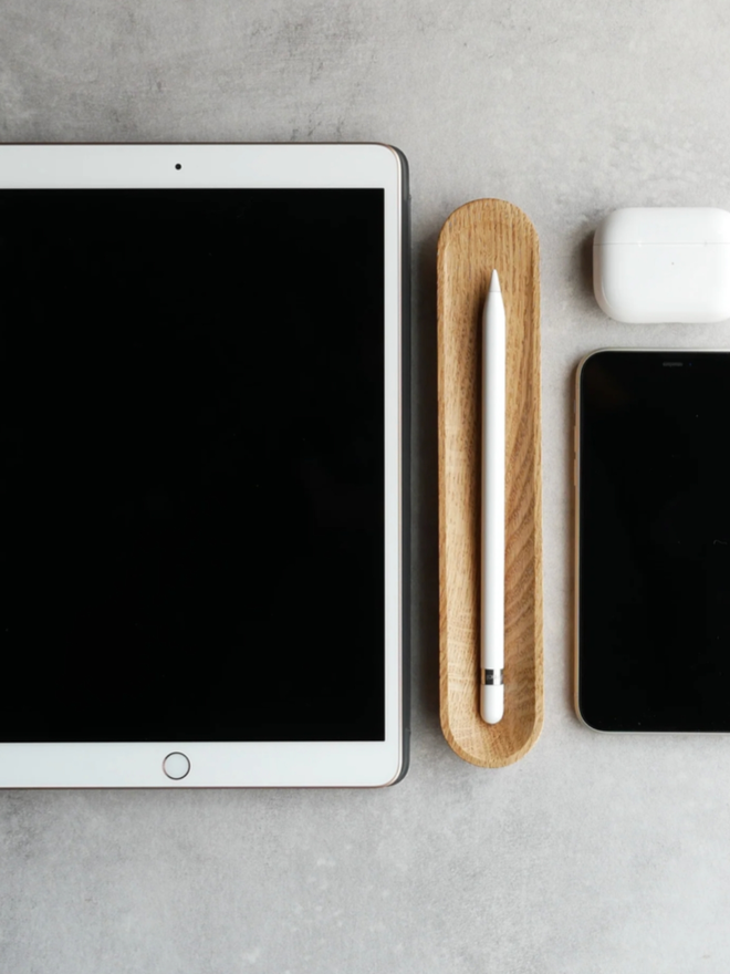 Pen Rest. The Oak variant showcased next to various pieces of tech. The pen holder contains an iPad stylus.