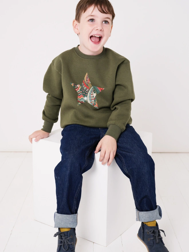 a 5 year old boy wearing a khaki christmas sweatshirt with a festive liberty print star appliquéd on the front