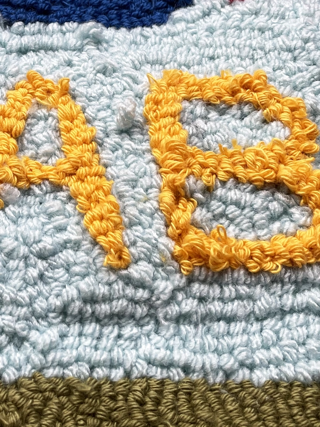 letter "A&B" in yellow loop pile wool on pale blue background