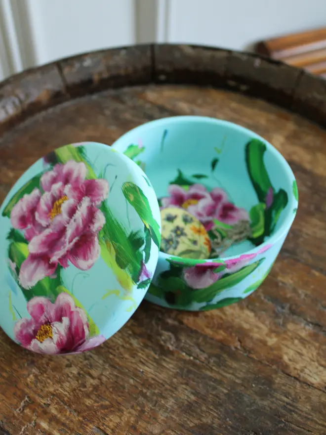 A beautifully hand painted floral ceramic round box background painted in a pale blue adorned in vibrant pink and white peony flowers.