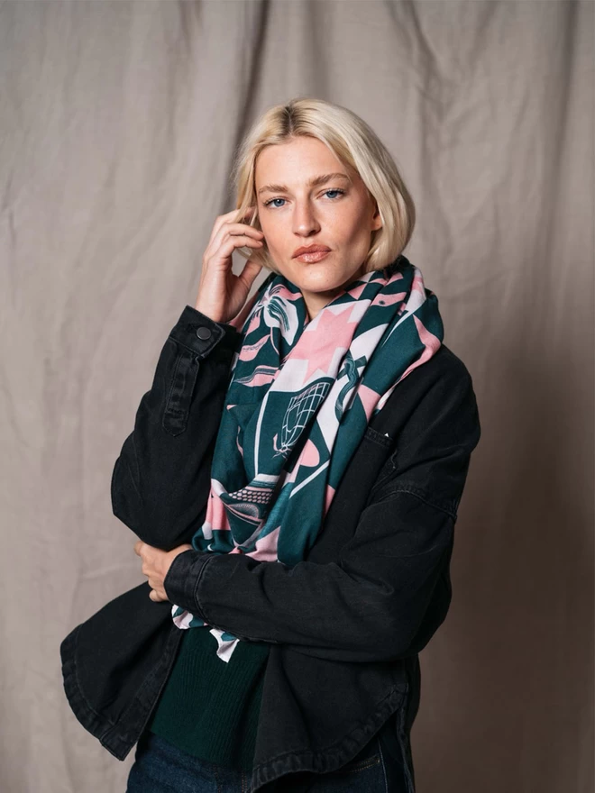 A model wears a large light weight forest green and calamine scarf displaying a range of motifs representing iconic women 