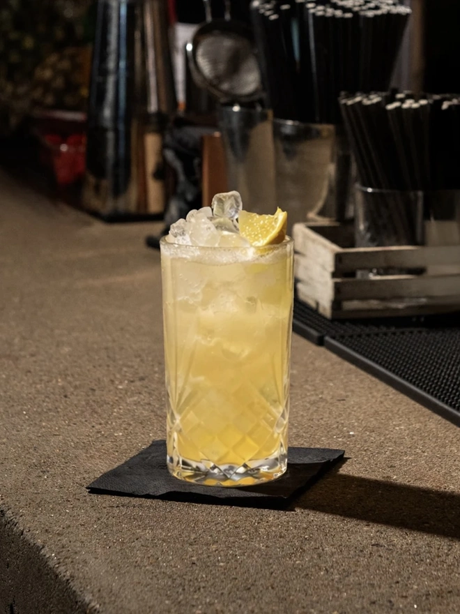 Sicilian Lemon Elixir, a drink sitting on a bar accompanied by other bar equipment. 