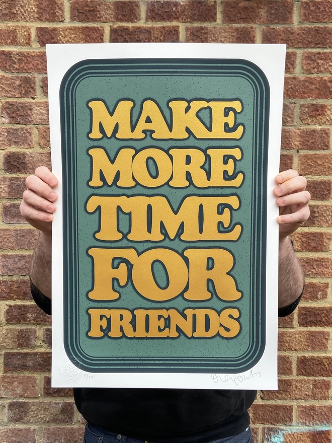 green leather looking screen print with gold letters that says “make more time for friends”