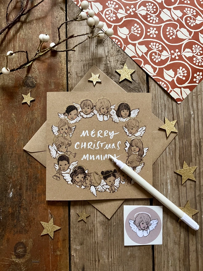 an illustrated Christmas card featuring a circle decorative angels all different ethnicities of children printed in black ink hand fished in white crayon and paint pens