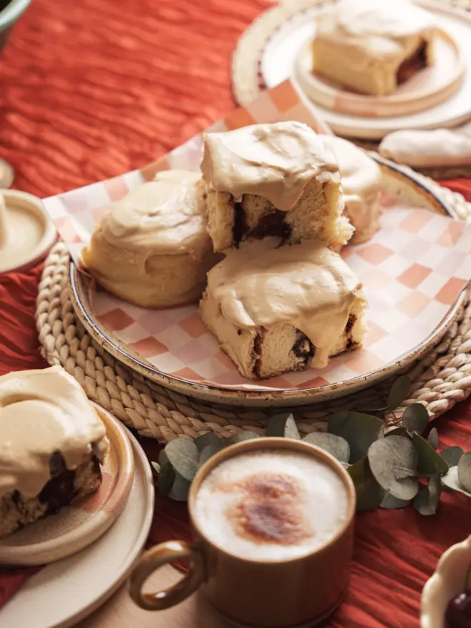 a stack of Latte Cinnamon Buns on a plate with checkerboard paper next to a latte coffee