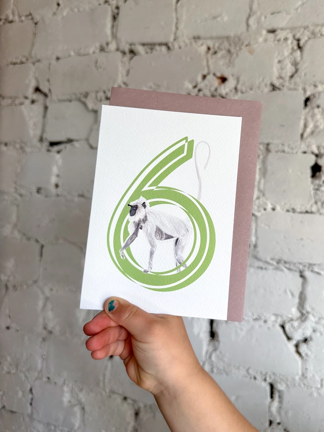 white card with a big green number 6 and an illustrated monkey with a purple envelope