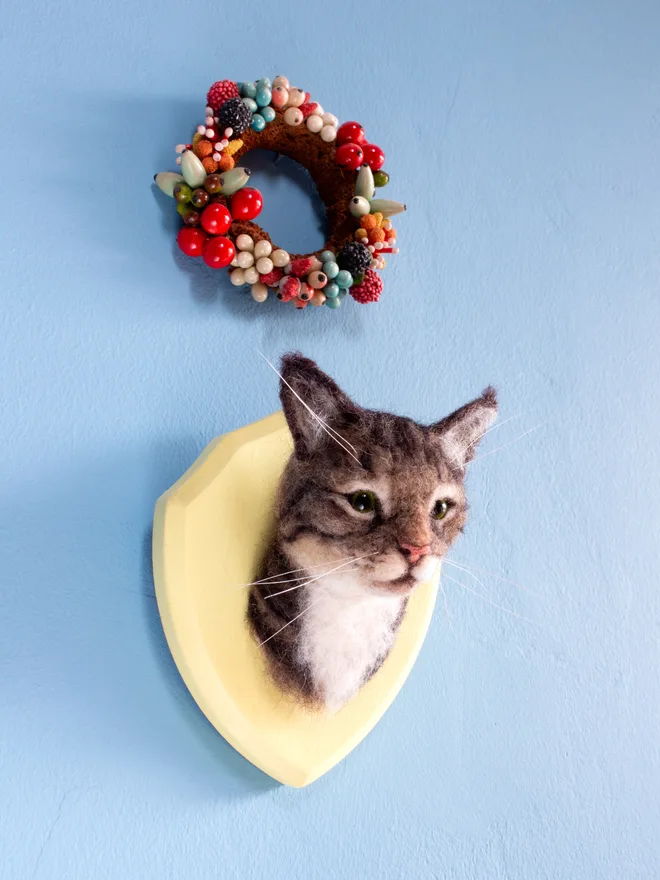 A handmade needle-felted tabby cat portrait mounted on a wooden shield