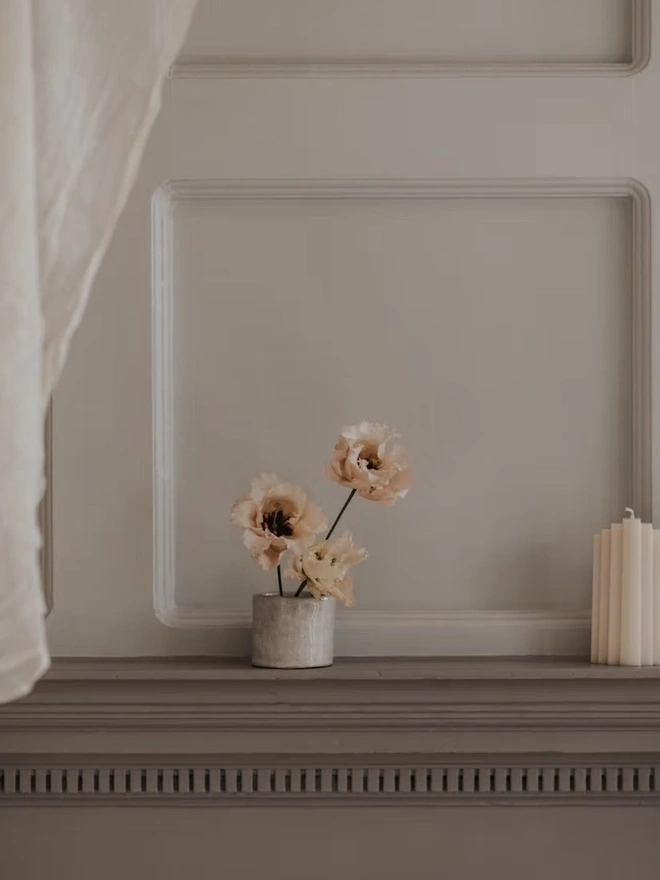 Ikebana, ceramic vase pictured with pink flowers on a ledge. 