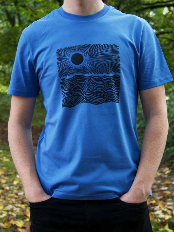 man wearing a blue t-shirt with a black handprinted design on the front depicting the sun and the sea