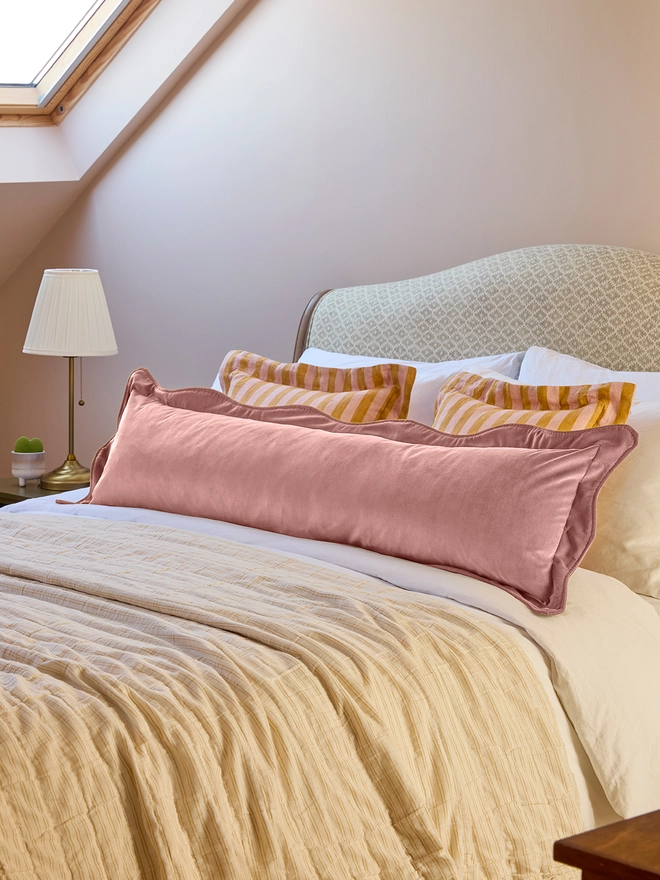 Handmade scalloped dusky pink velvet bolster cushion 130cm with feather pad paired with stripe linen cushions on bed, Kika Bespoke