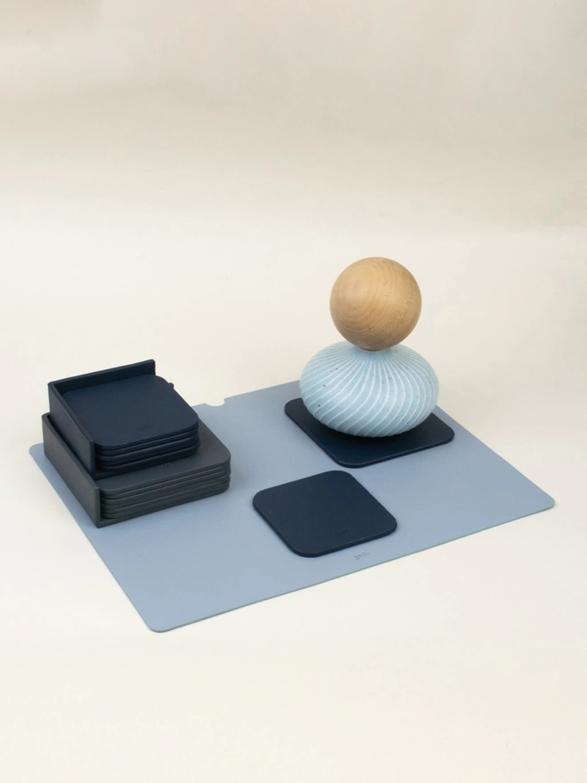 Grey and Blue Coasters styled on an Ice blue placemat. There is a sky blue circular vase on the left top corner of the placemat on a navy coaster.