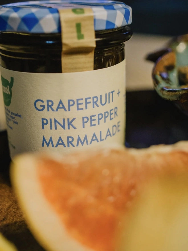 Jar Of Grapefruit & Pink Peppercorn Marmalade, jar of marmalade on a plate next to a slice of grapefruit. 