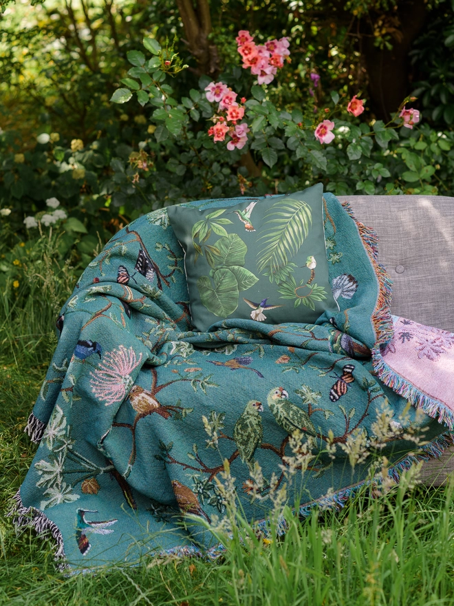 Forest Flight Blanket by Arcana seen outside on a pink sofa.