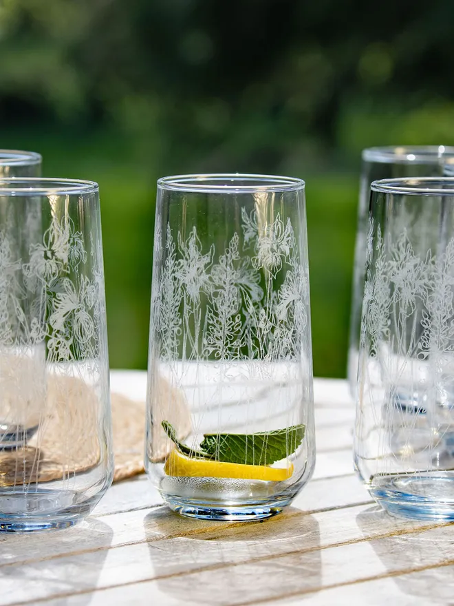 A set of tall, floral-etched highball glasses on an outdoor table.