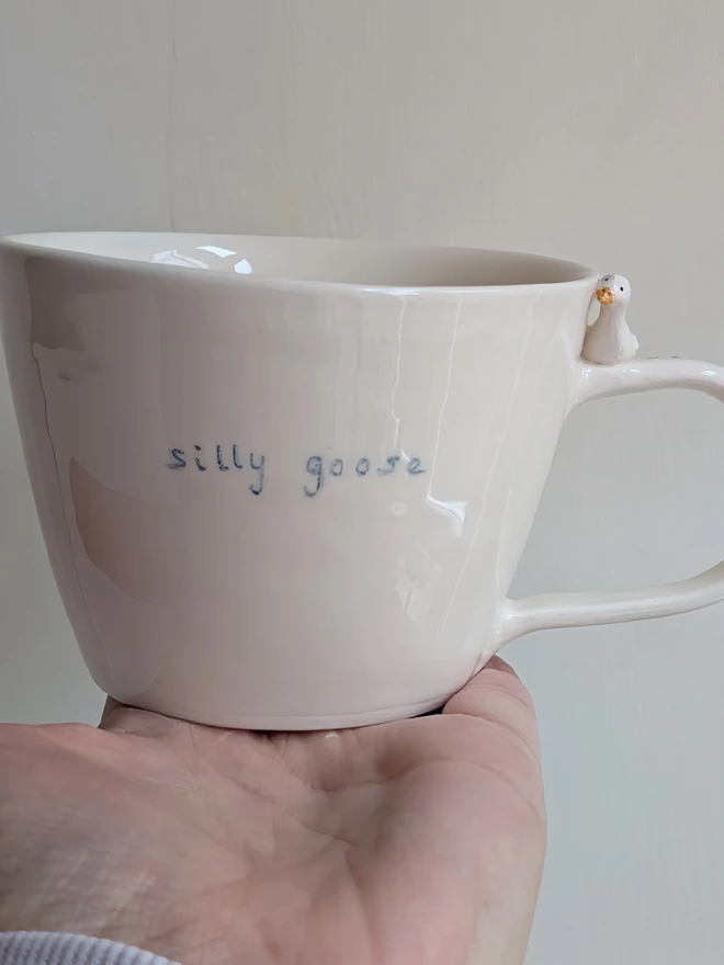 white handmade ceramic goose cup with a tiny bird, bird prints and the words silly goose handpainted in blue simple font