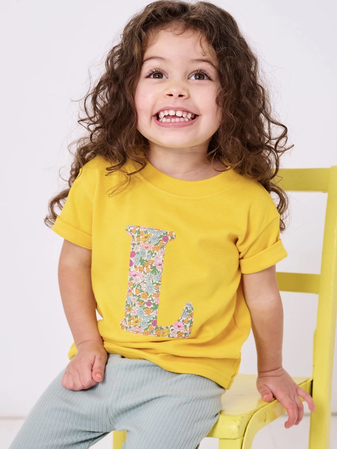 little girl in yellow t-shirt with floral initial on front