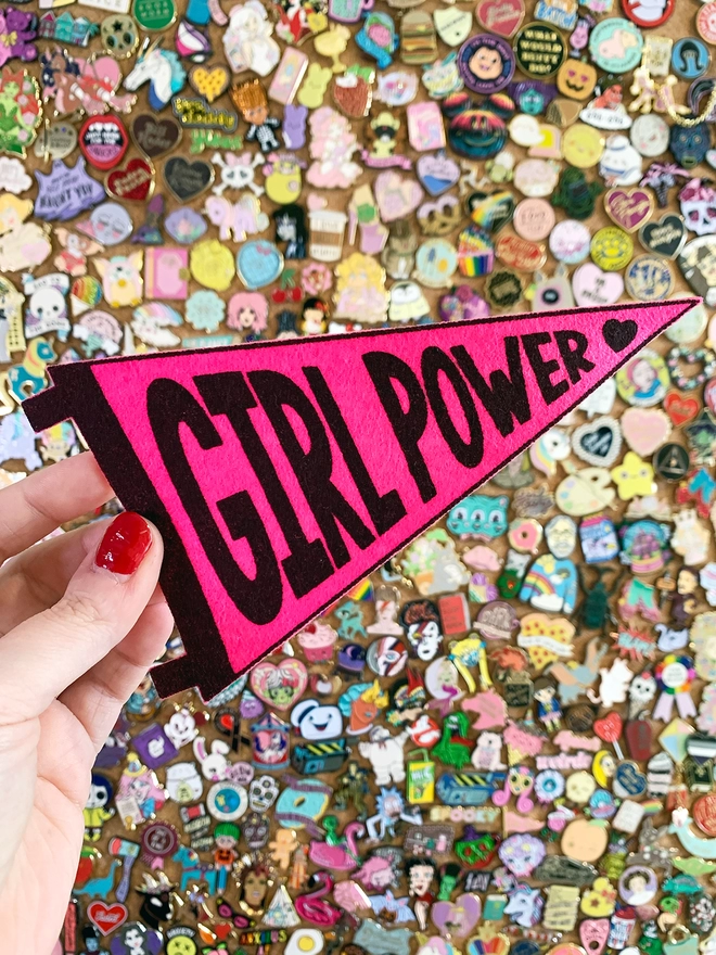 image shows a hand holding a small felt pennant with the words 'Girl Power' printed in black ink on hot pink felt.