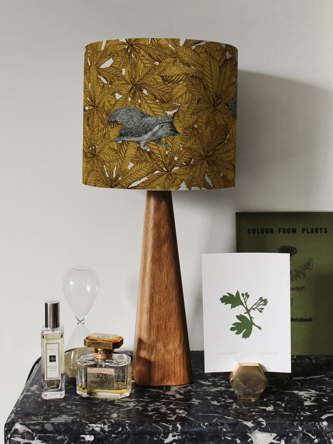 Handmade lampshade featuring cosy hedgehogs nestled among autumnal yellow leaves, creating a warm and whimsical woodland design.