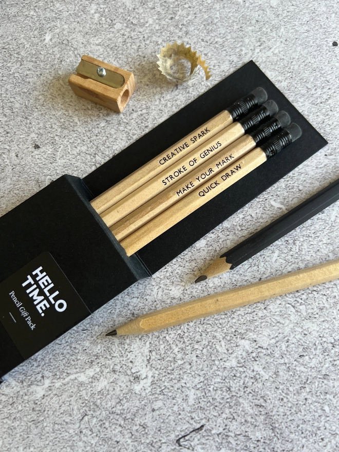 Four natural wood pencils each with a different quote in a card sleeve along side a pencil sharpener