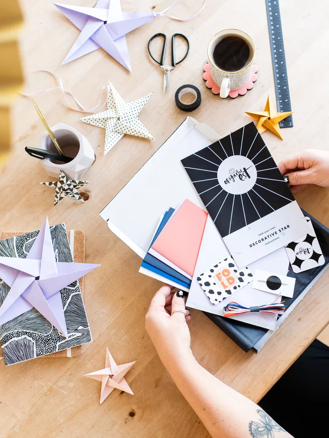 Woman holding origami kit with origami stars scattered on table
