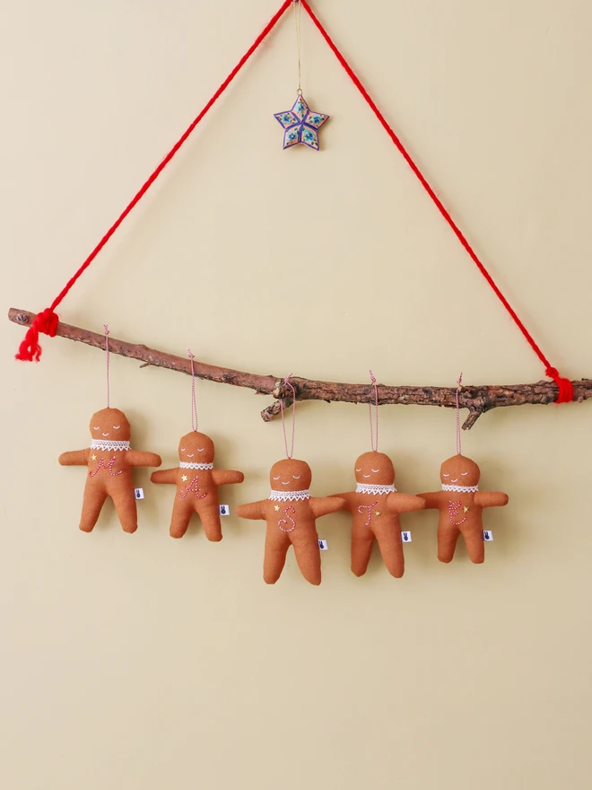Brown linen gingerbread man christmas tree ornament with a letter hand embroidered in candy cane colours, star shaped sequin, crochet cotton lace around the neck, smile embroidered in white and candy cane colour string to hang. 