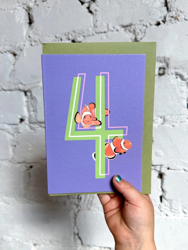 a purple card with a big green number 4 and two clown fish illustrations and a green envelope
